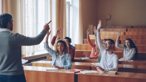 Teacher pointing at students with raised hands in lecture hall
