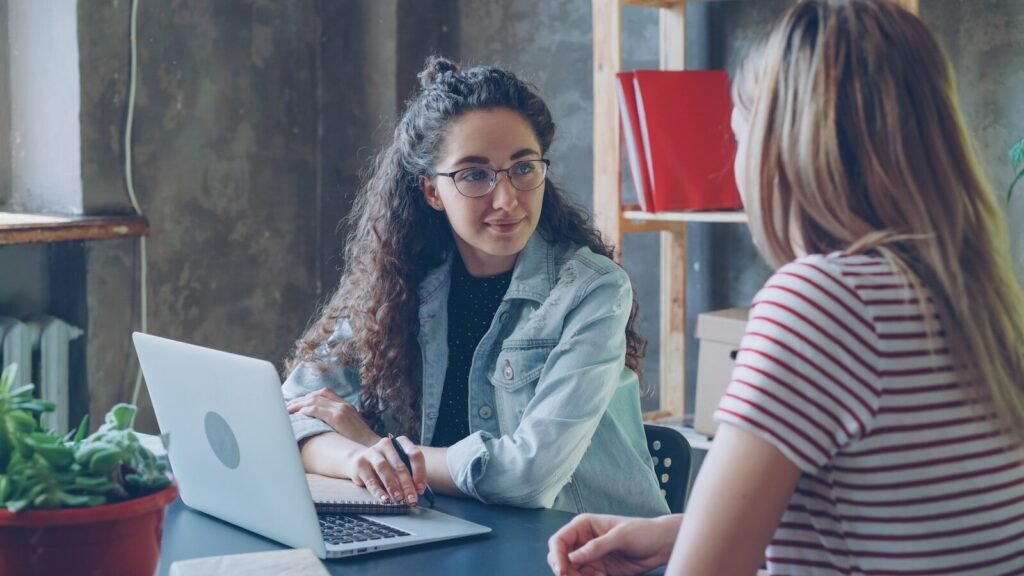 Two women are having a conversation at a desk